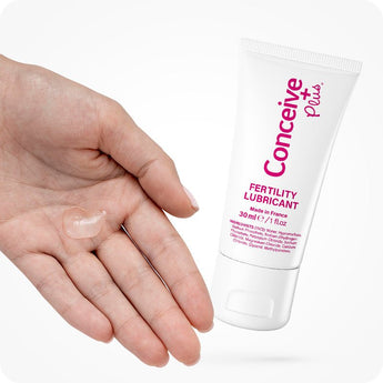 For Conceive Plus Try Me Size Bundle (30ml Tube and 3x4g Applicators), a close-up of a clear fertility lubricant gel dispensed onto an open palm, alongside 30ml fertility lubricant tube angled diagonally to display branding and ingredients, set against white background.
