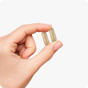 For Conceive Plus Women's Fertility Support and Ovulation Support Bundle, capsule detail photo showing two beige vegan ovulation capsules held between fingers, demonstrating compact size and smooth texture, captured against a white background.